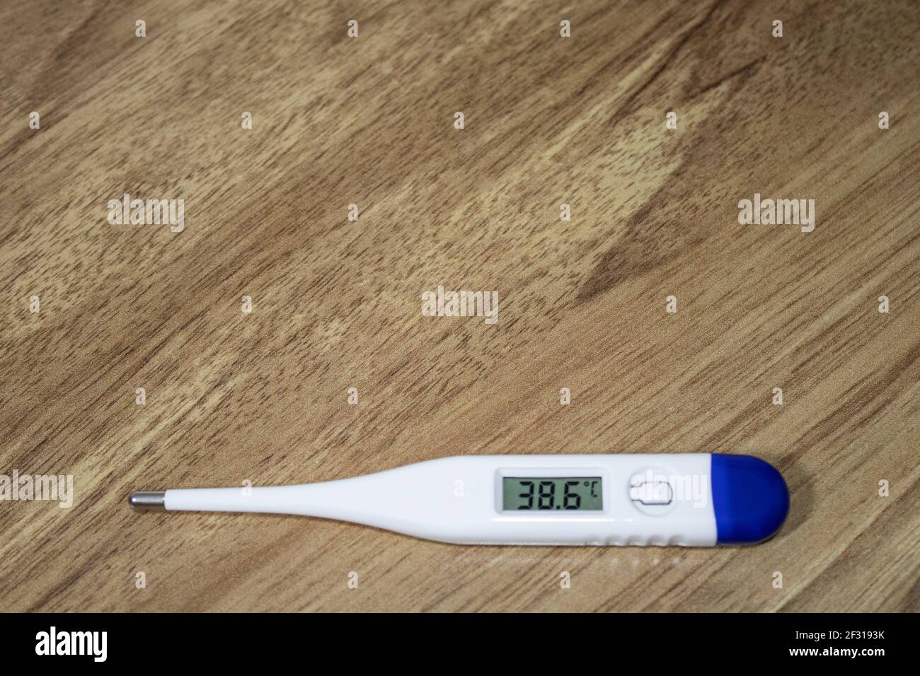 Thermometer with a blue handle and indicating 38 degrees, standing on a wooden table. High fever indicator. Stock Photo