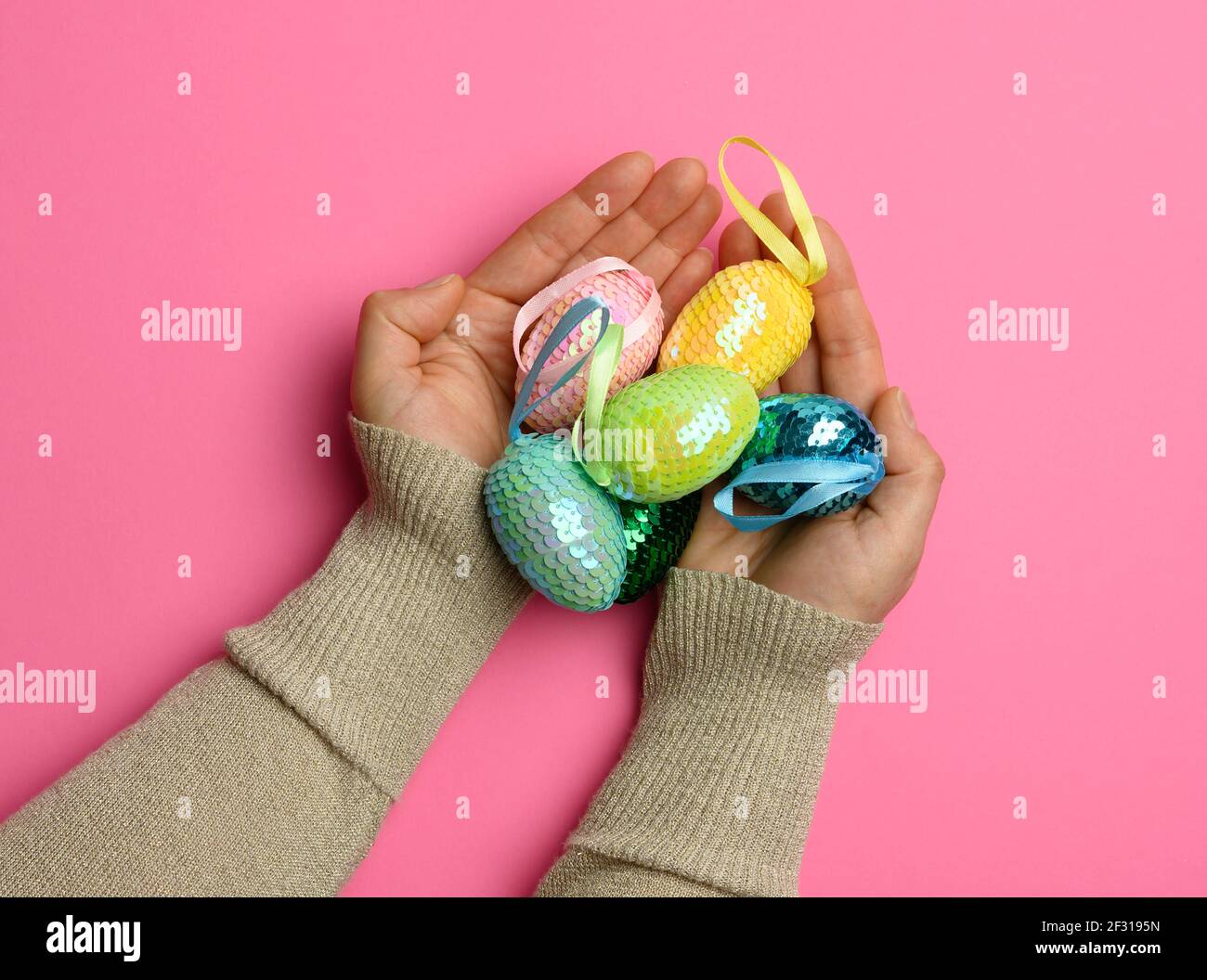 Female hand holding multicolored decorative easter eggs on pink background Stock Photo