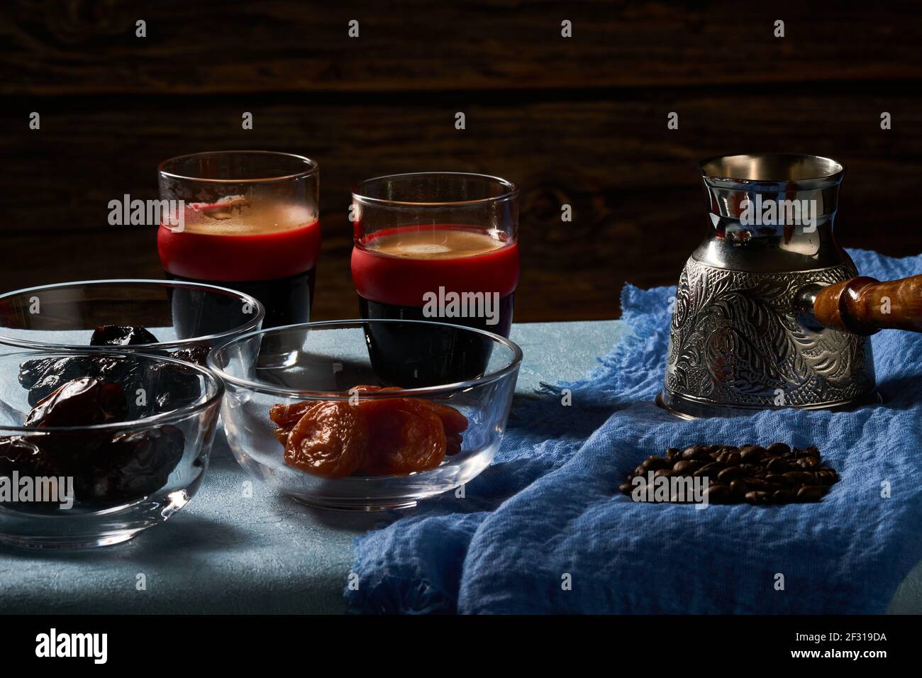 Coffee pot (Cezve), coffee beans, two glasses of coffee, dry apricot and dry plum. Stock Photo