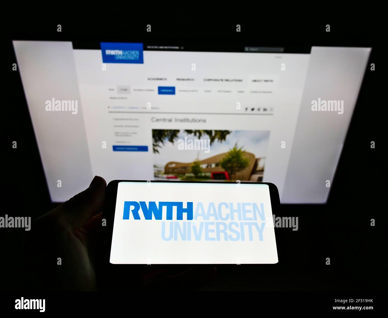 Person holding smartphone with logo of German education institution RWTH Aachen University on screen in front of webpage. Focus on phone display. Stock Photo