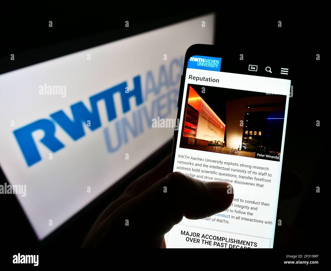 Person holding mobile phone with logo of German education institution RWTH Aachen University on screen in front of web page. Focus on phone display. Stock Photo