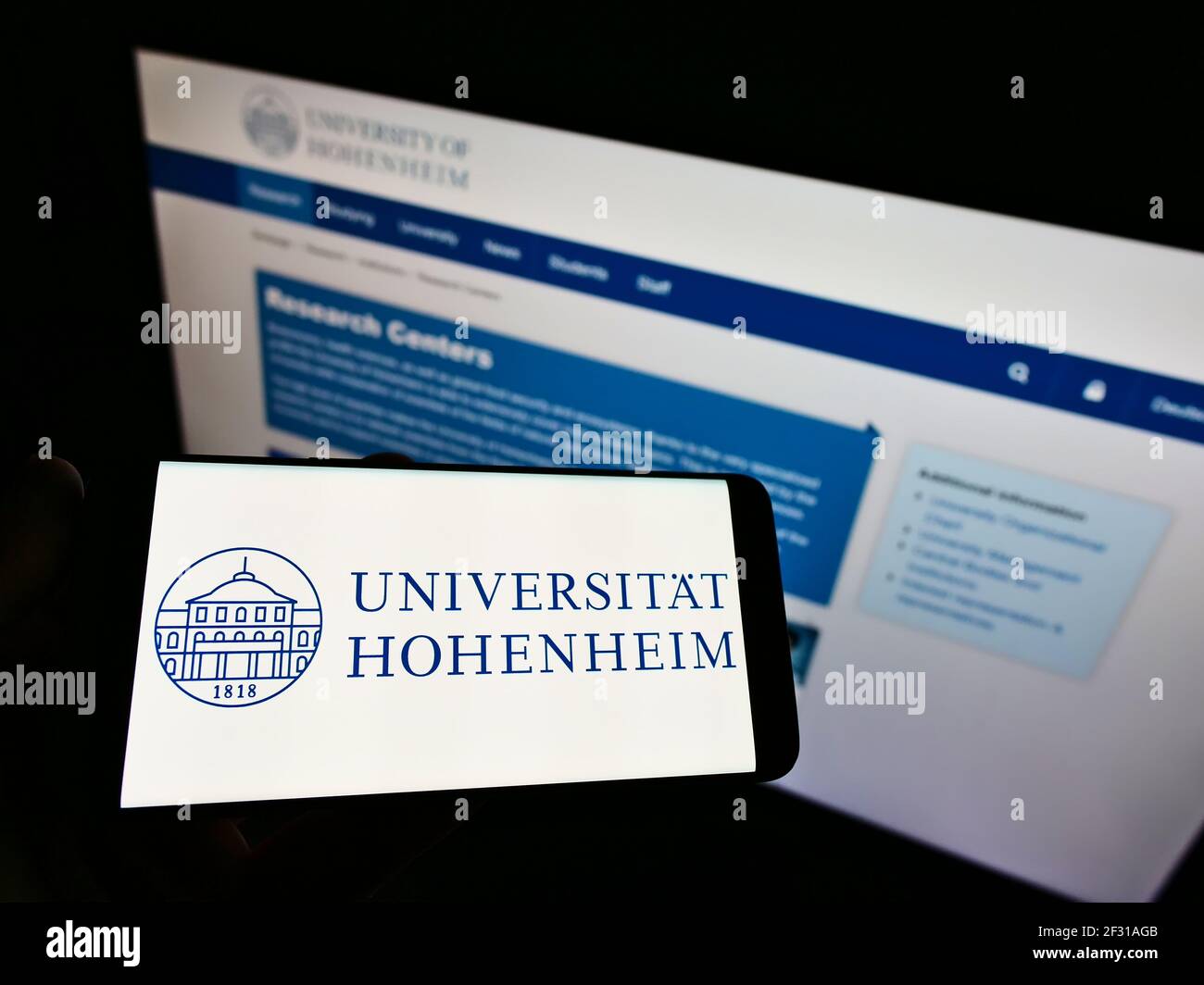 Person holding cellphone with logo of German university Universität Hohenheim (Stuttgart) on screen in front of webpage. Focus on phone display. Stock Photo