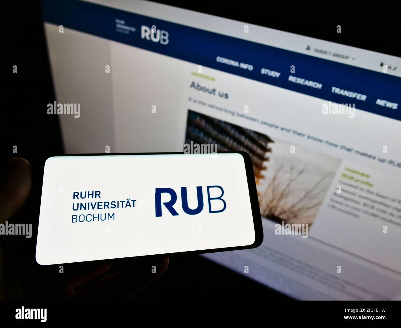 Person holding smartphone with logo of German university Ruhr-Universität Bochum (RUB) on screen in front of website. Focus on phone display. Stock Photo