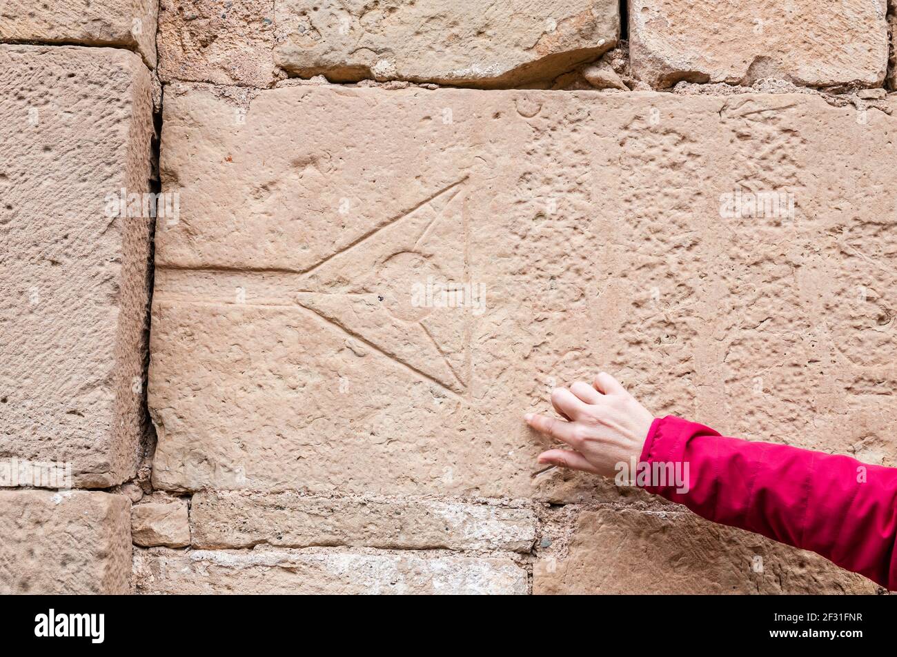 woman pointing geometric symbols on stone wall, Santa Maria church, Talamanca, Catalonia, Spain Stock Photo