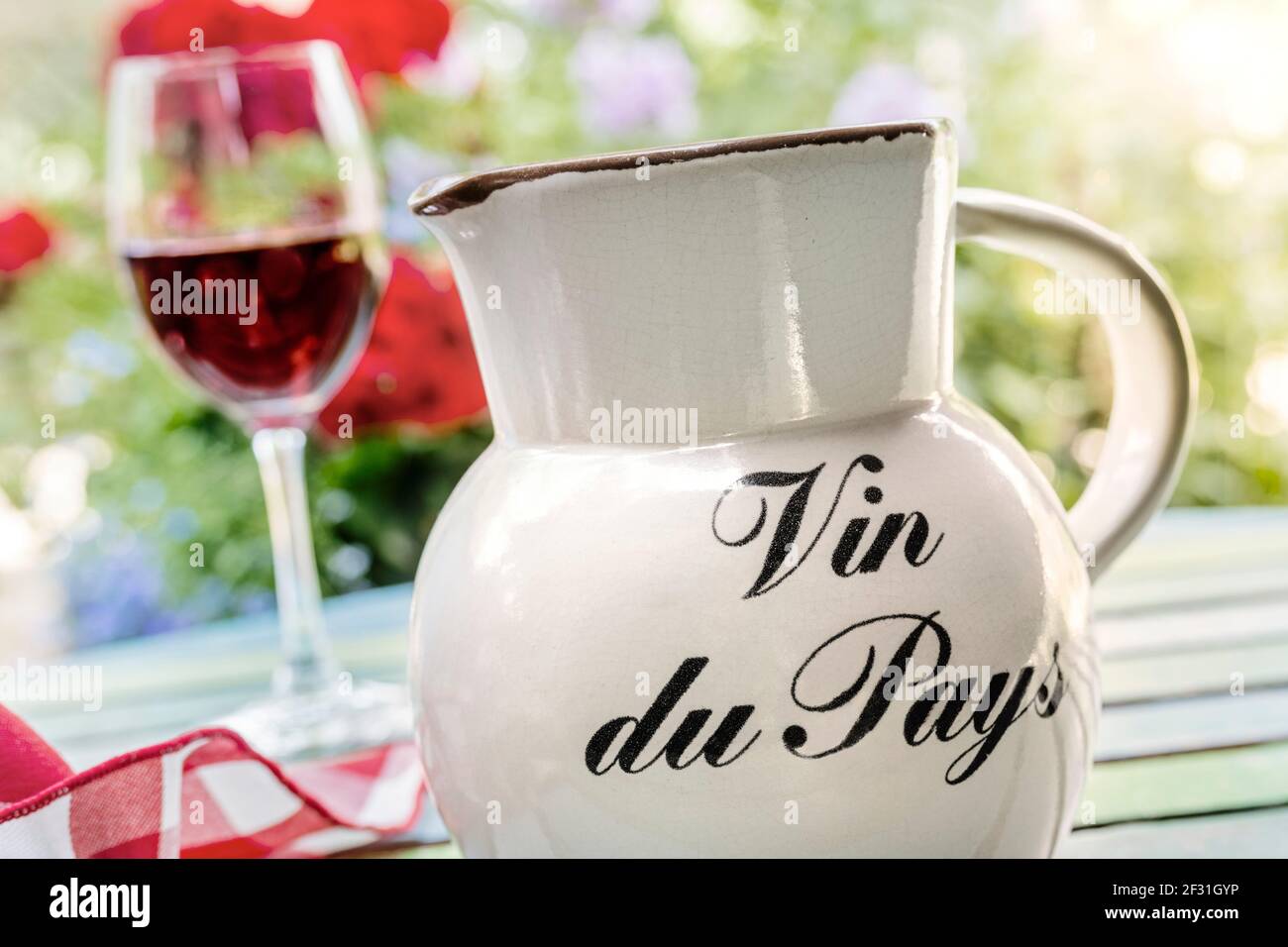 Vin du Pays table wine jug and glass of simple French country red wine on holiday alfresco terrace table with floral garden sunset Gites de France Stock Photo