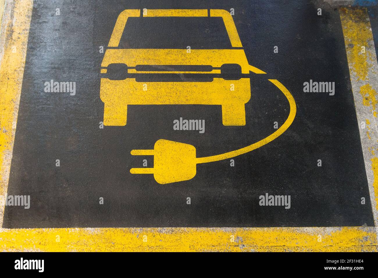 Line markings in a car parking bay in yellow on black tarmac of a car and electric charging lead are visible. Stock Photo