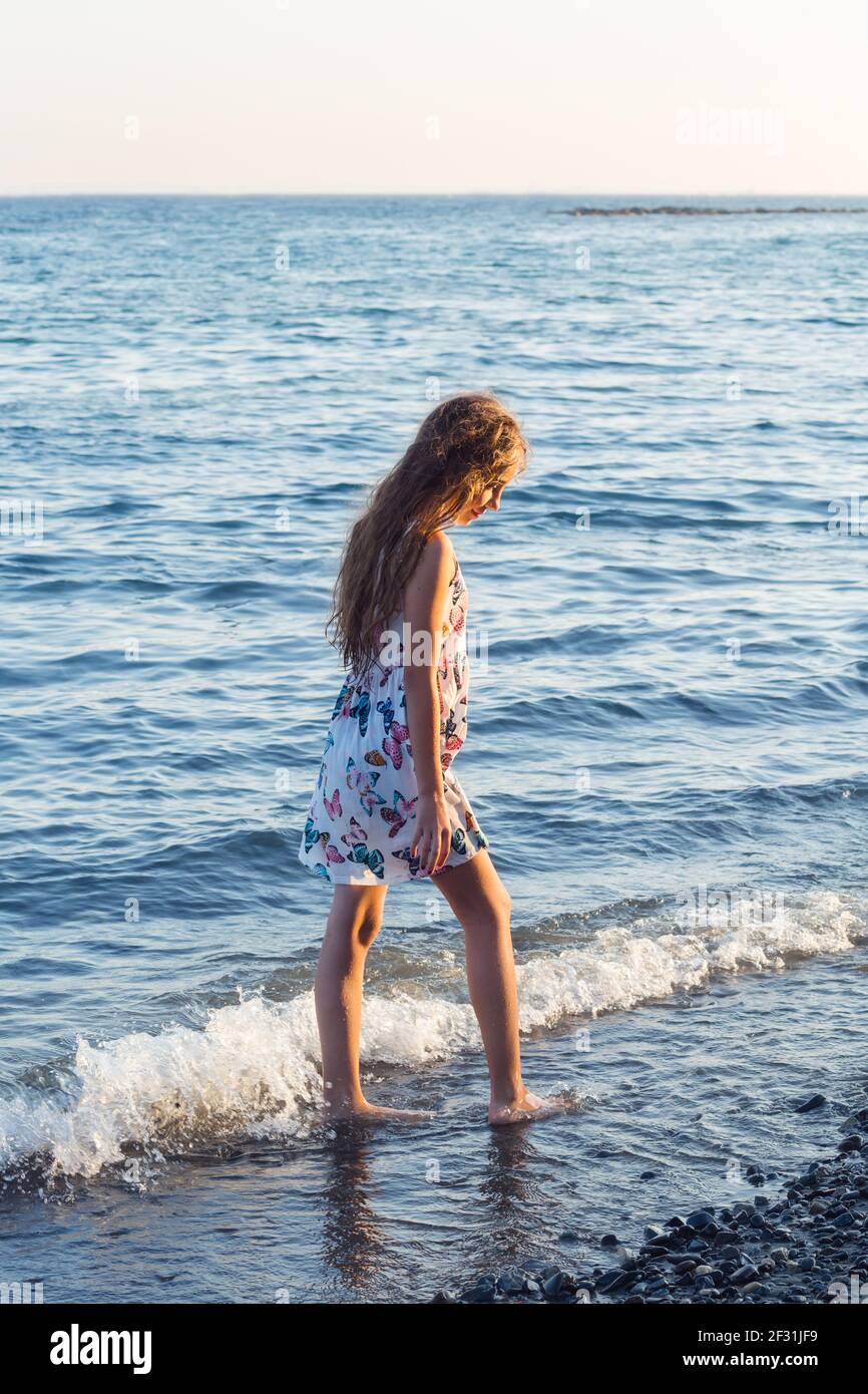 Beautiful teen Girl is playing with waves by the Sea at sunset.  Summer Sunny Day, Ocean Coast, happy Kids concept Stock Photo