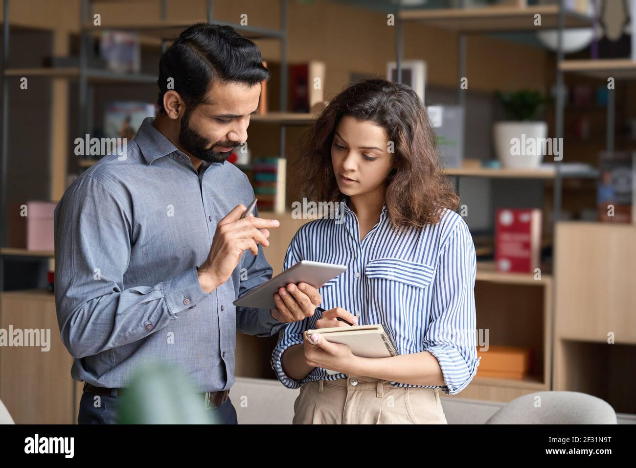 Indian manager holding digital tablet having discussion with latin employee. Stock Photo