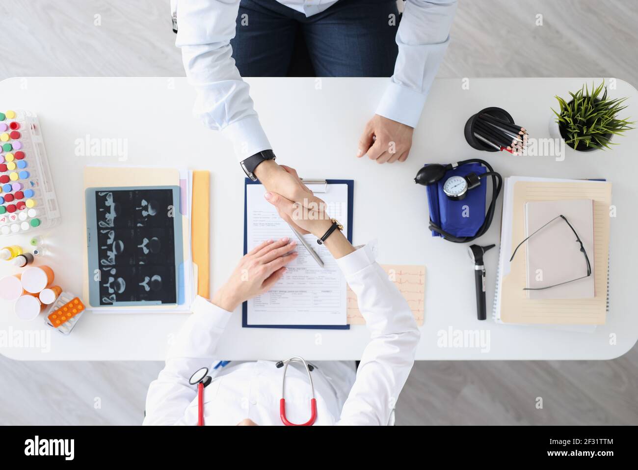 Doctor and patient shake hands in handshake at medical table Stock