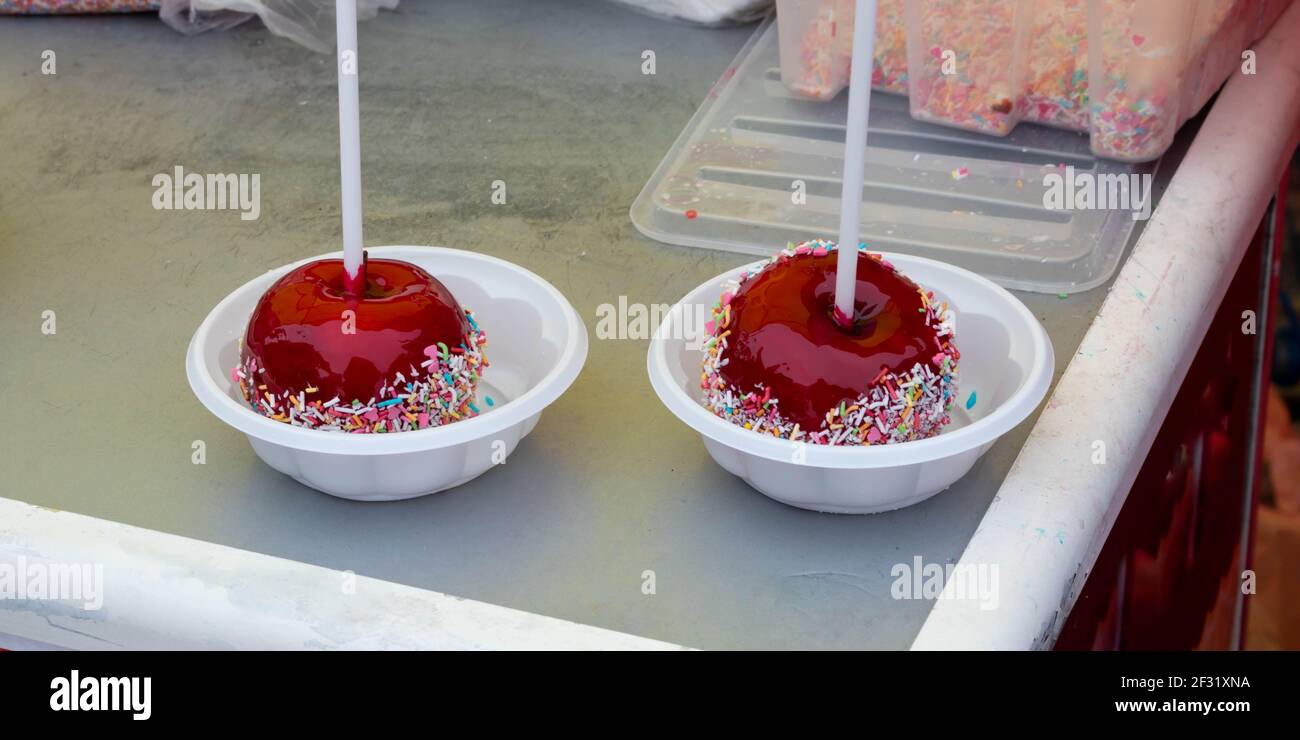 A red caramelized apple on a stick, covered in hard red sugar, standing in a plastic plate to serve as a festive treat. The concept of Easter, Masleni Stock Photo