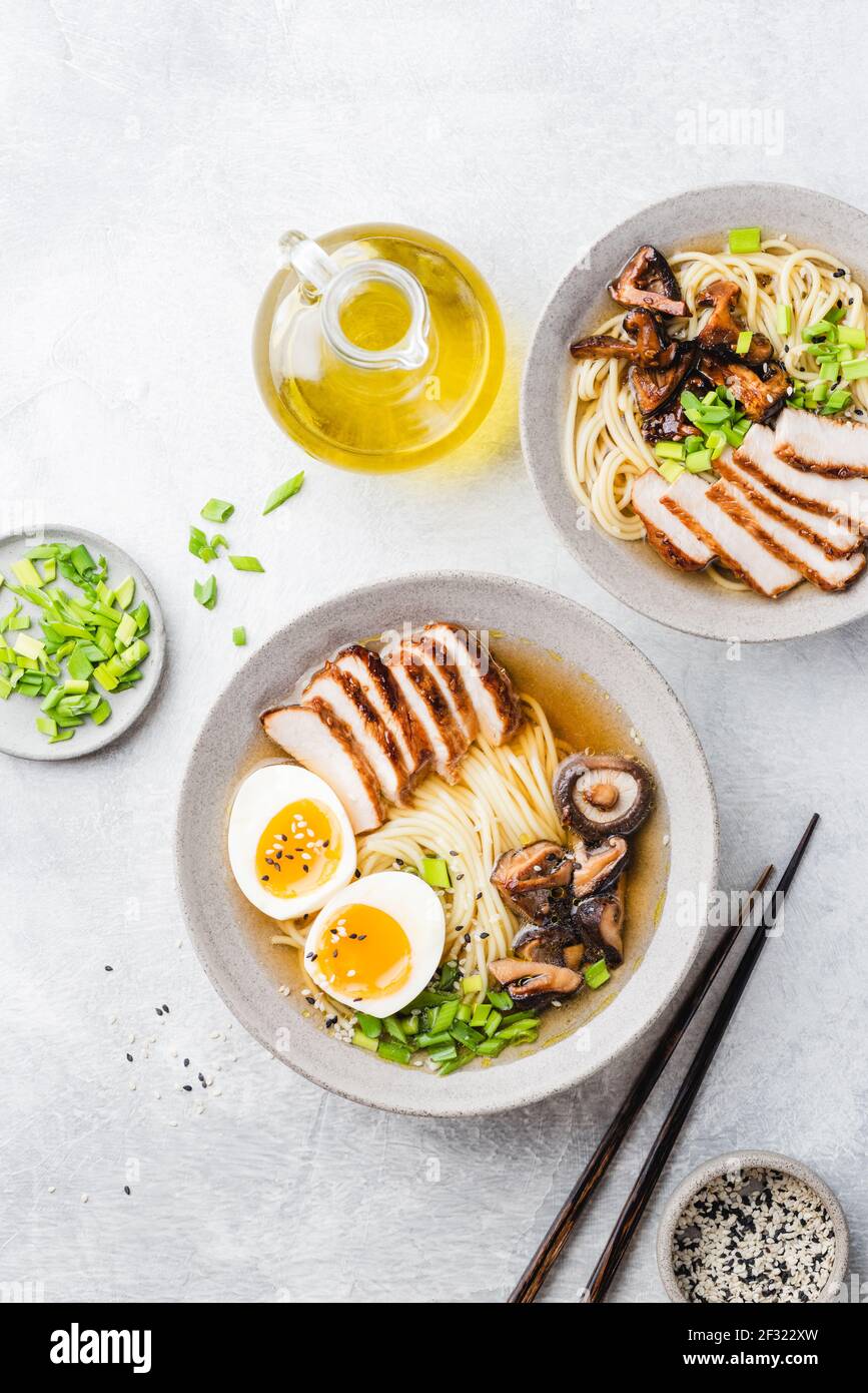 Asian noodle soup ramen with chicken and shiitake mushrooms on grey concrete background, table top view. Two bowls of Ramen Stock Photo