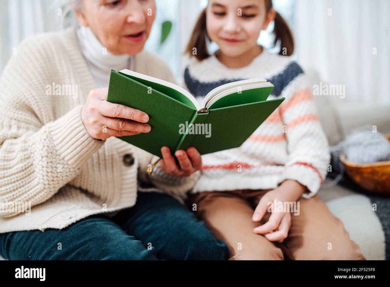 Good granny sitting on a couch with her granddaughter. they are reading a book together. Focus on the object, faces blurred. Stock Photo