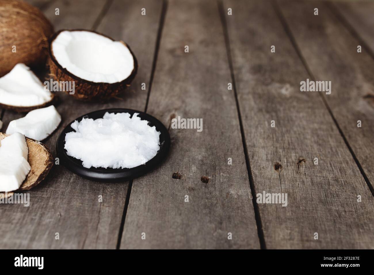 Broken coconuts on gray wooden background. White coconut fresh pulp on black plate. High quality photo Stock Photo