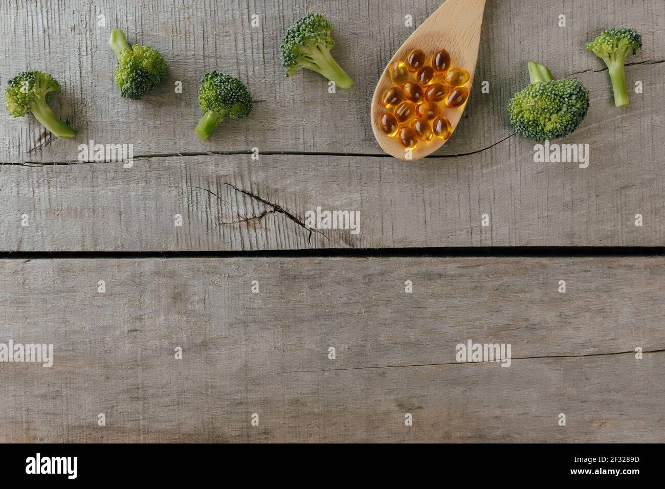 Flat lay with omega 3 capsules on wooden spoon, broccoli on wooden background. Natural medicine, health concept. Vitamin pills. High quality photo Stock Photo