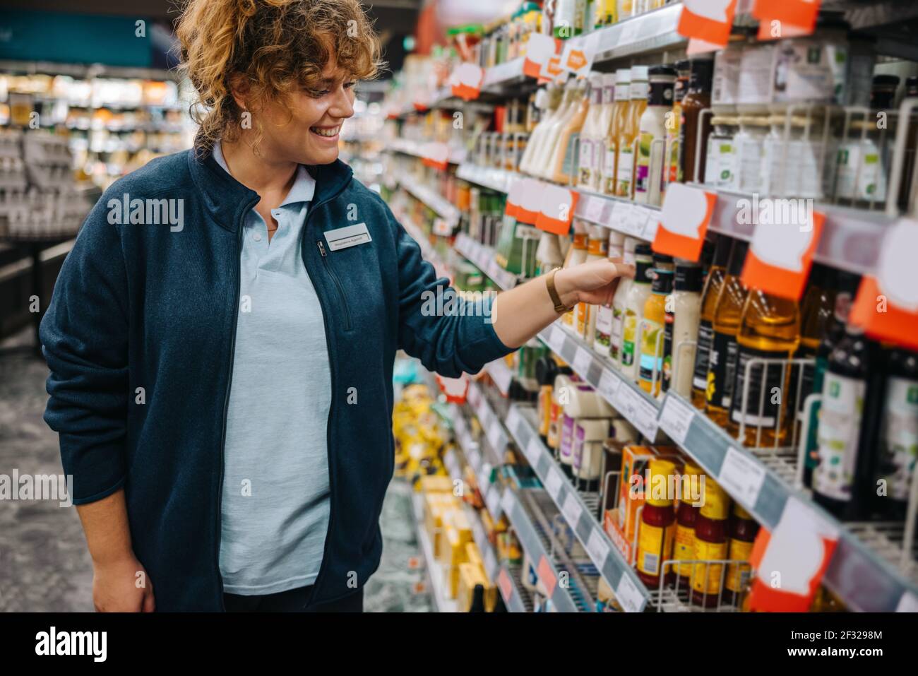 Woman working in supermarket. Female employee arranging the products correctly on the rack and smiling. Stock Photo