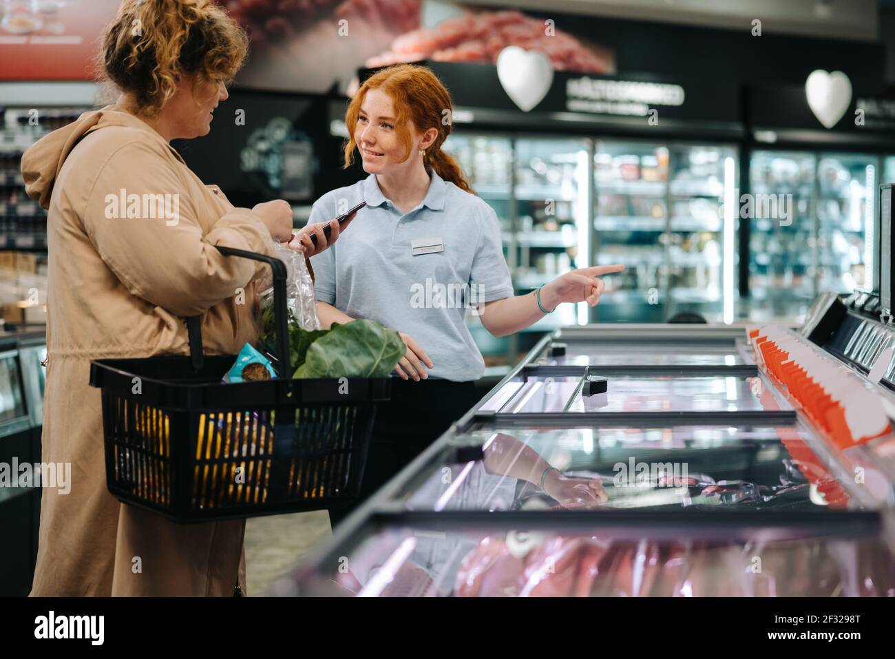 Young shop assistant helping female customer in grocery store. Saleswoman assisting shopper in supermarket. Stock Photo