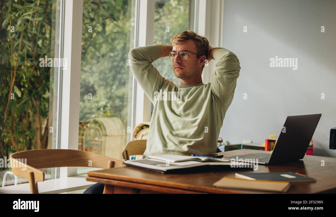 Man sitting at table with hands behind head. Man taking break while working from home. Stock Photo