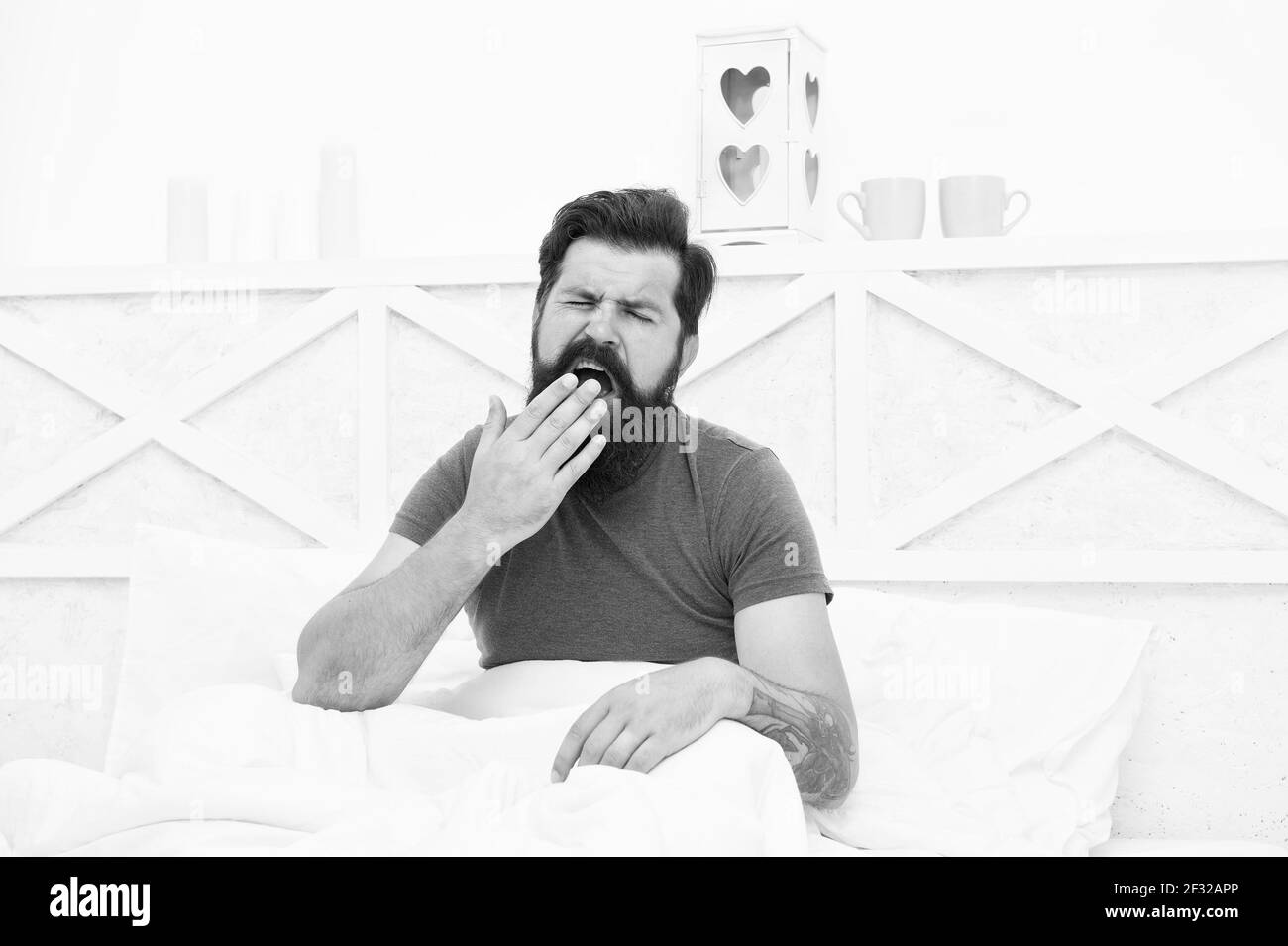 Lethargic tired man sitting in bed yawning as he struggles to wake up unmotivated to start the new day, early morning routine Stock Photo