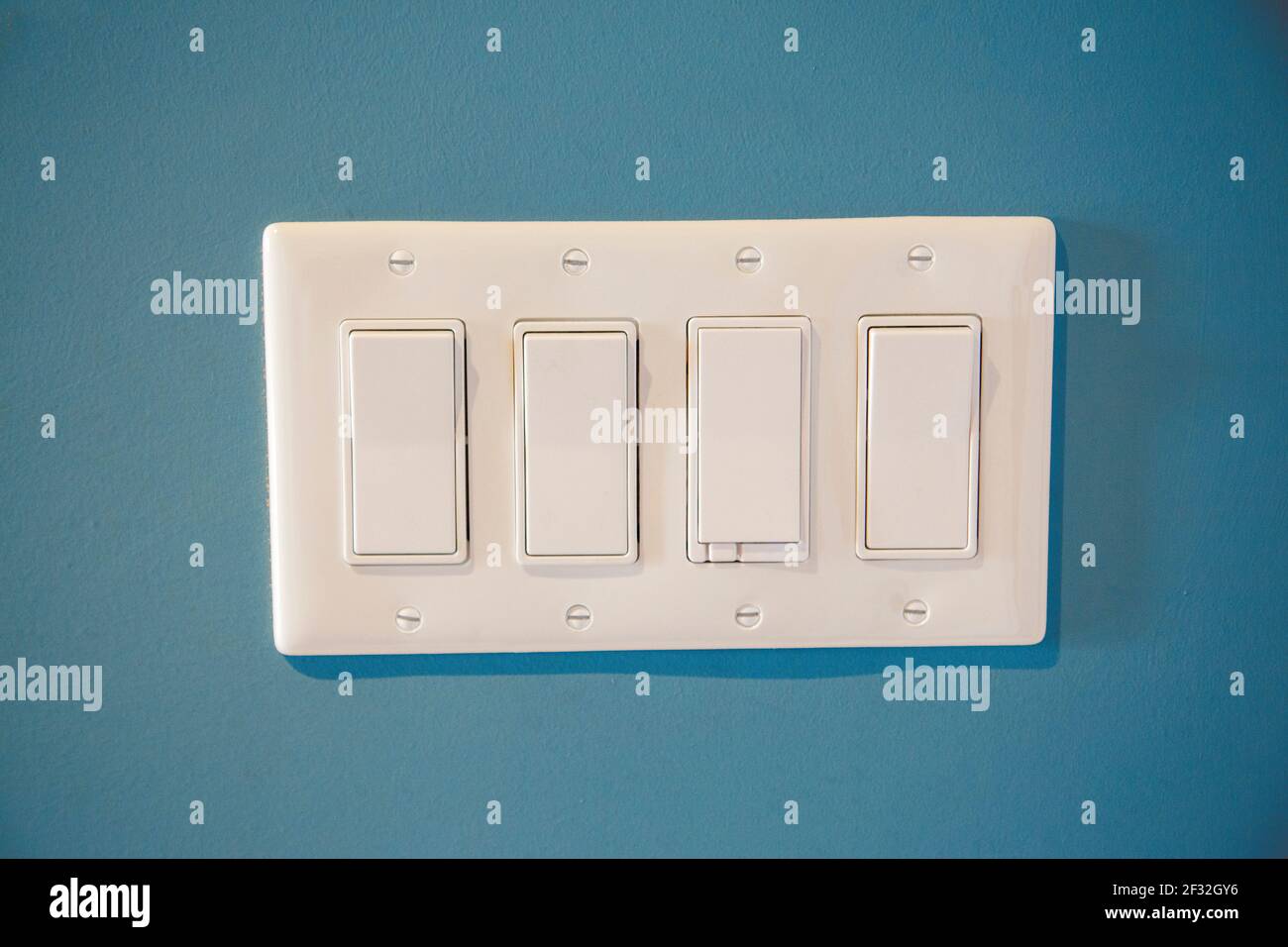 a blue wall with a panel of light switches flipped to on and off positions inside a house Stock Photo