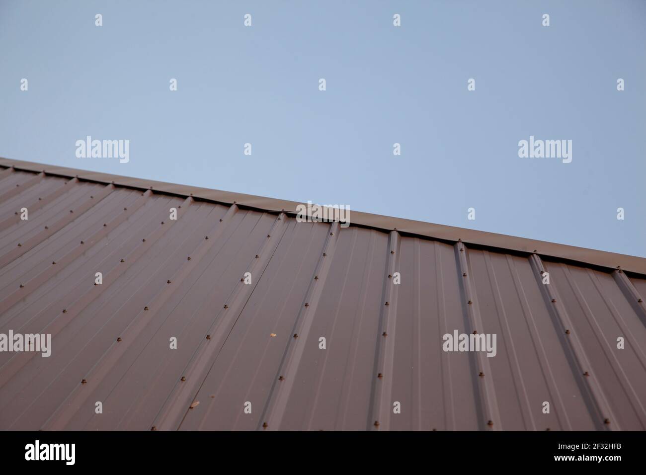 a new metal roof with bolts cuts diagonally across the frame against a clear blue skyline Stock Photo