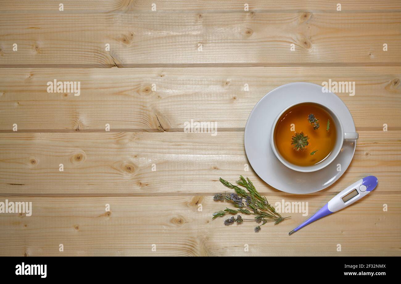 A cup and saucer of thyme herbal tea and a thermometer next to it. Flat lay on a wooden table top. Stock Photo