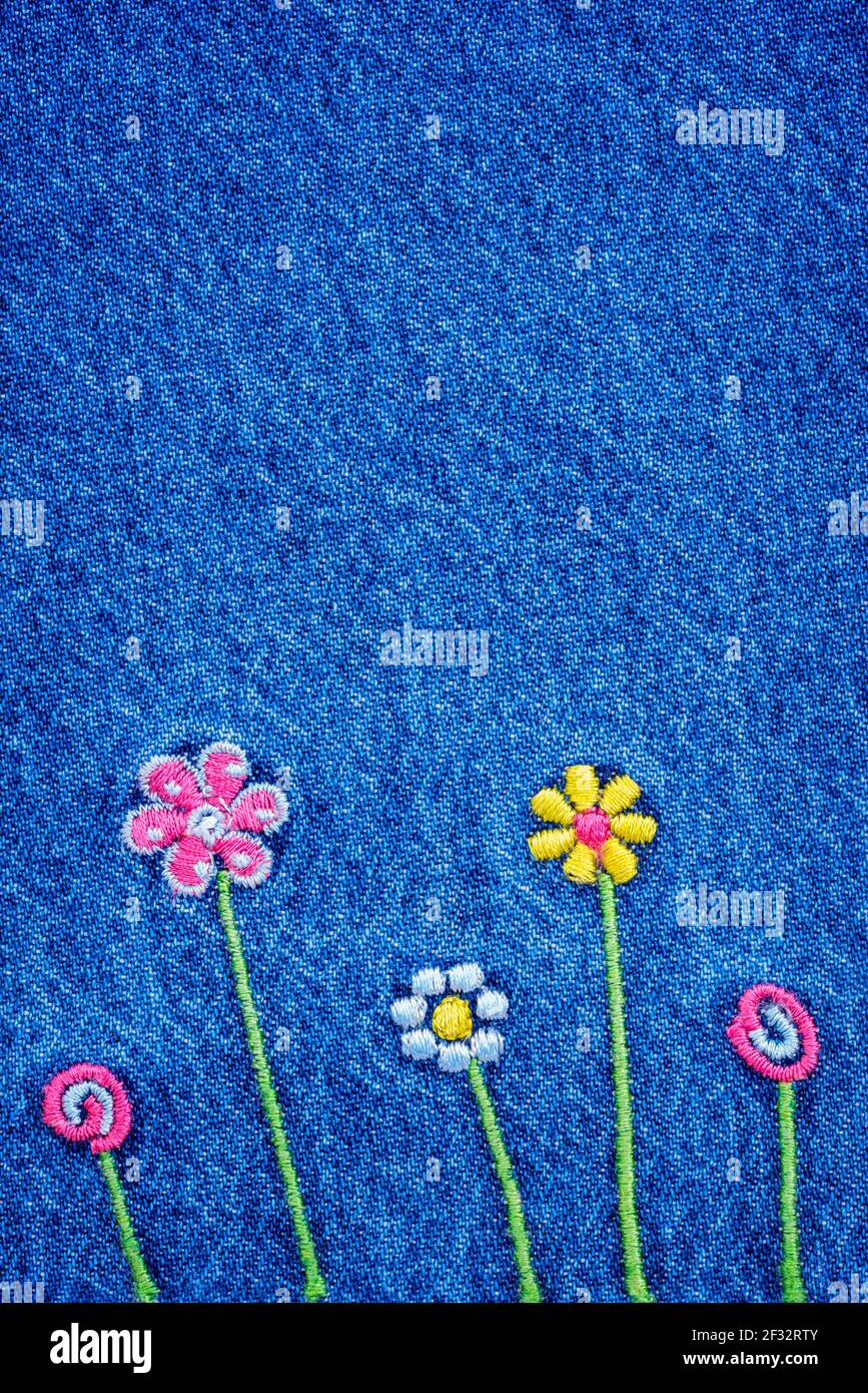 Embroidered 5 flowers on fragment of  blue denim jeans texture Stock Photo