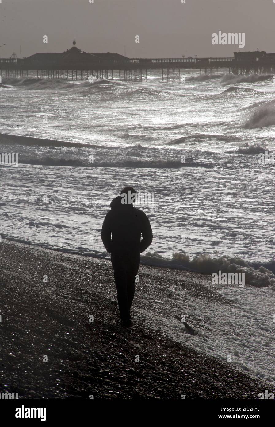 Man walking along Brighton beach on a stormy morning, with the silhouetted shape of the Pace Pier beyond. Brighton & Hove, East Sussex, England, UK. Stock Photo