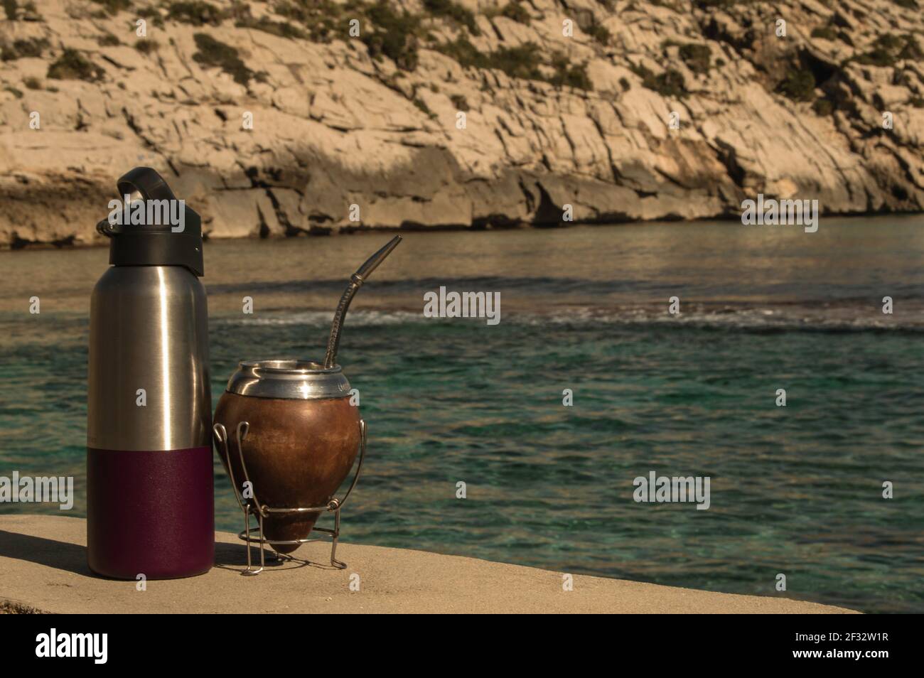 Mate y termo en la playa- Drinking Mate on the rocks. Mediterranean beach with transparent turqoise water. Good feeling. Helthy life style Stock Photo