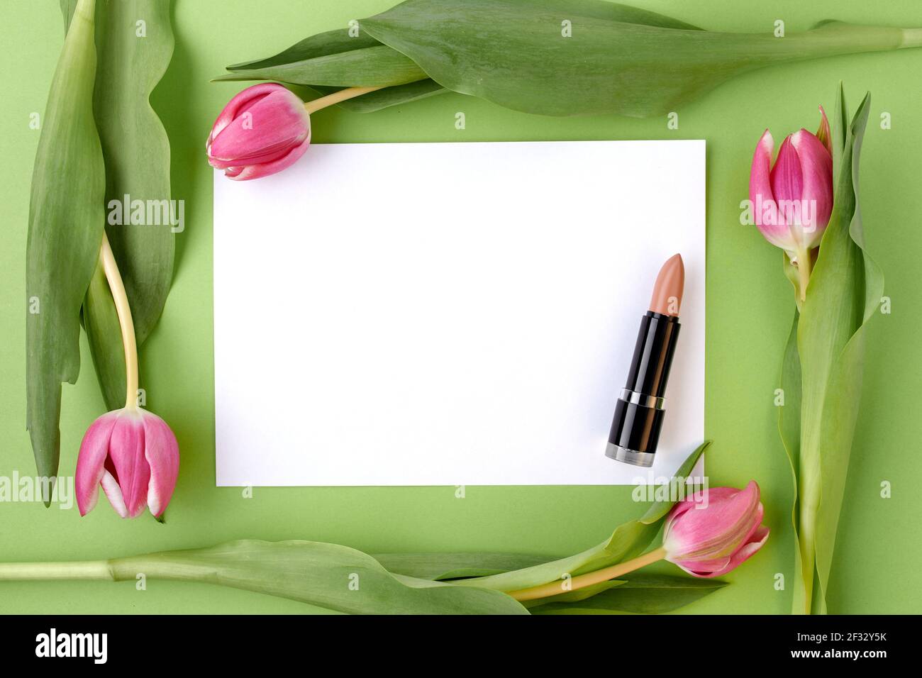 spring flat lay with lipstick, paper sheet and tulips isolated on green ...