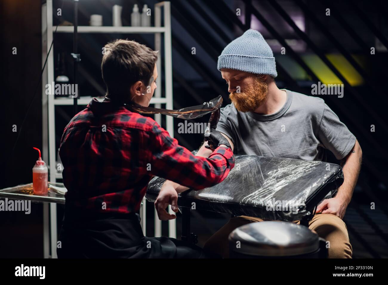 In a modern tattoo parlor, a girl with piercings and tattoos on her body makes a tattoo on the