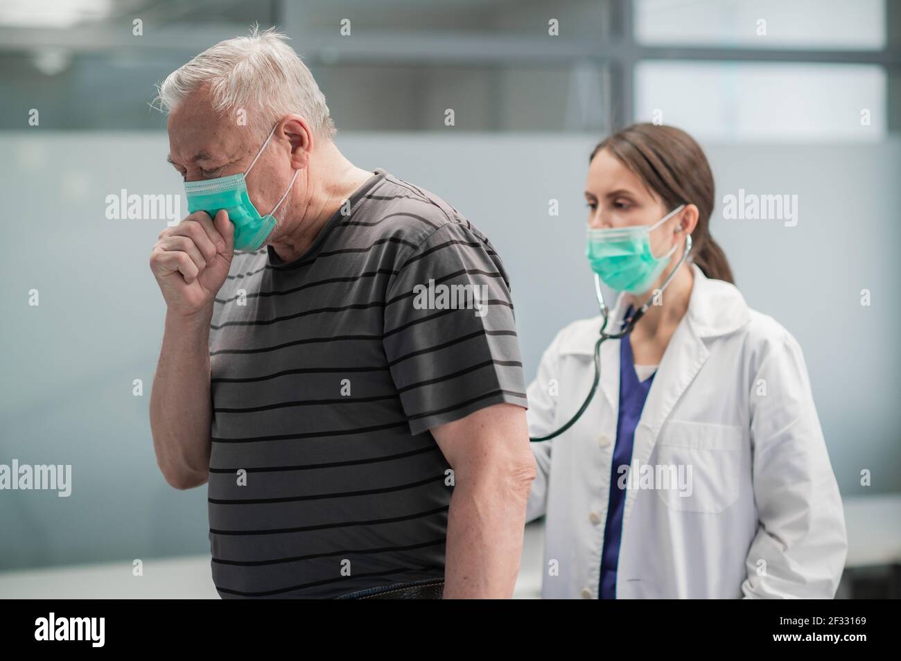 Cute female doctor listens to the lungs of her elderly patient, he is sick and coughs Stock Photo