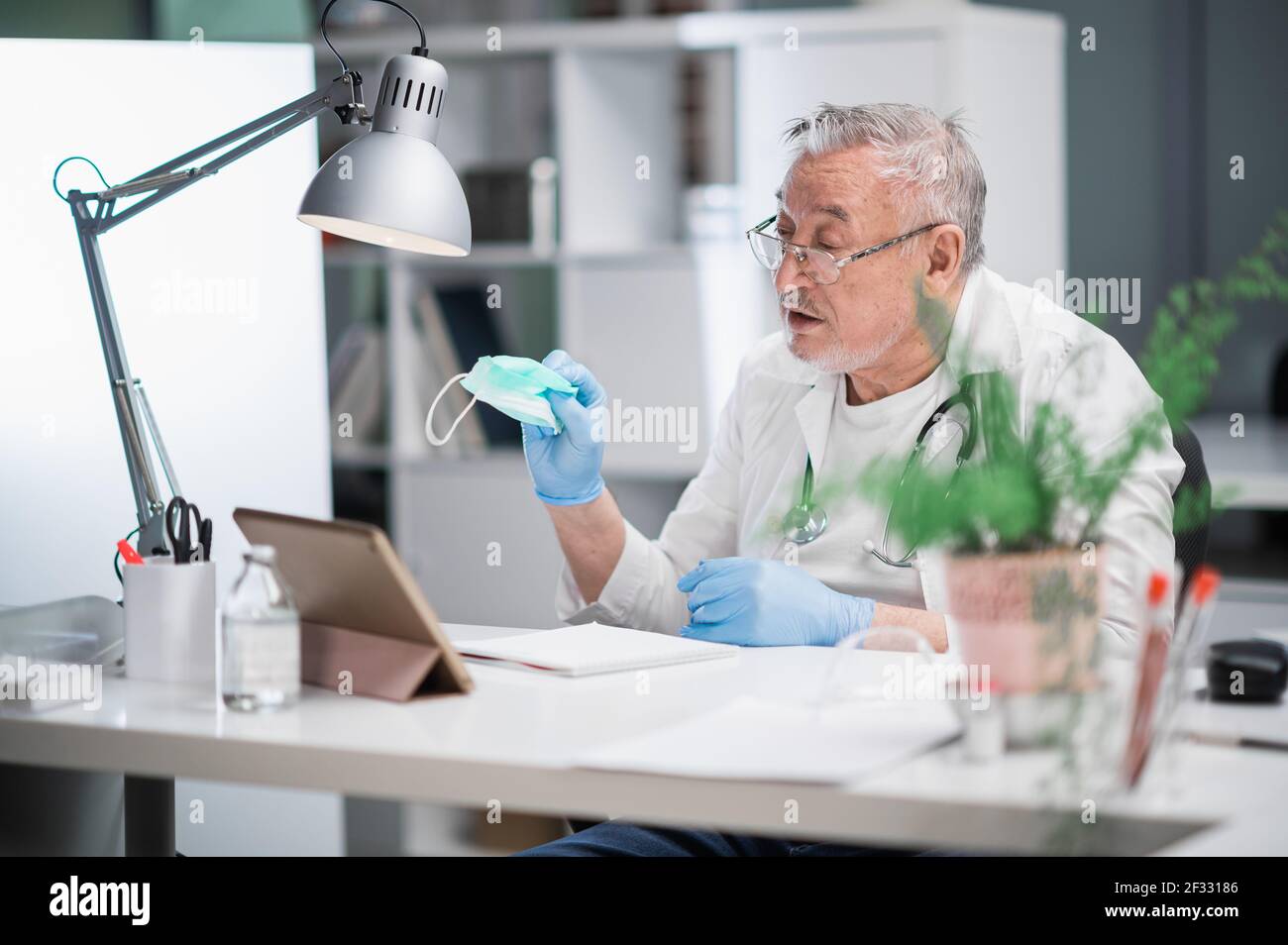 An elderly experienced doctor online explains to the patient the benefits of wearing a medical mask. Concept of online consultation with a medical Stock Photo