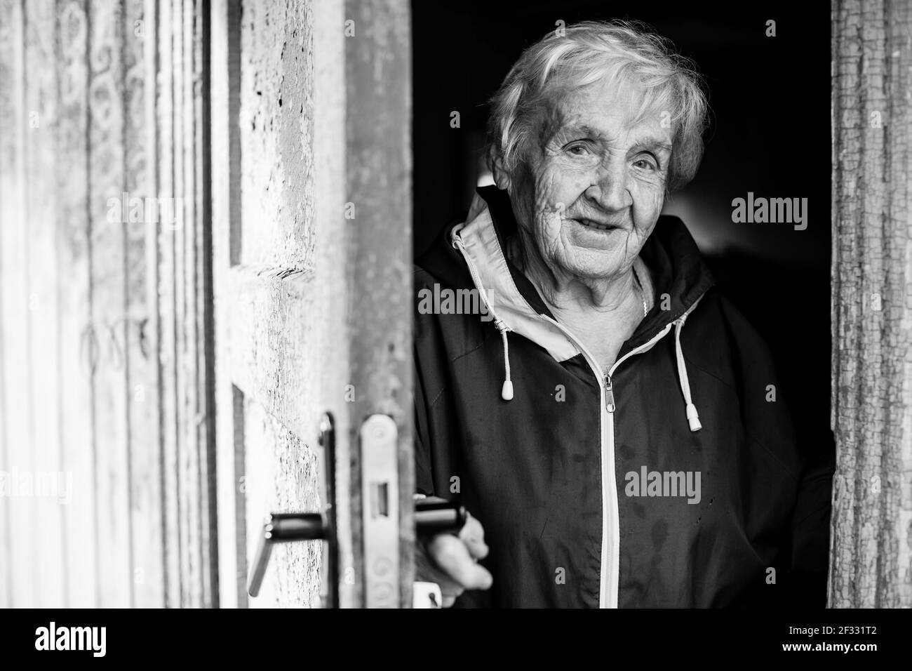 An old woman peeks out from behind door of house. Black and white photo. Stock Photo