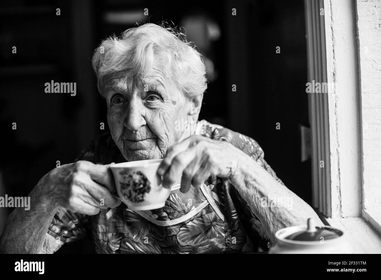 An old woman sitting at the table. Black and white photo. Stock Photo