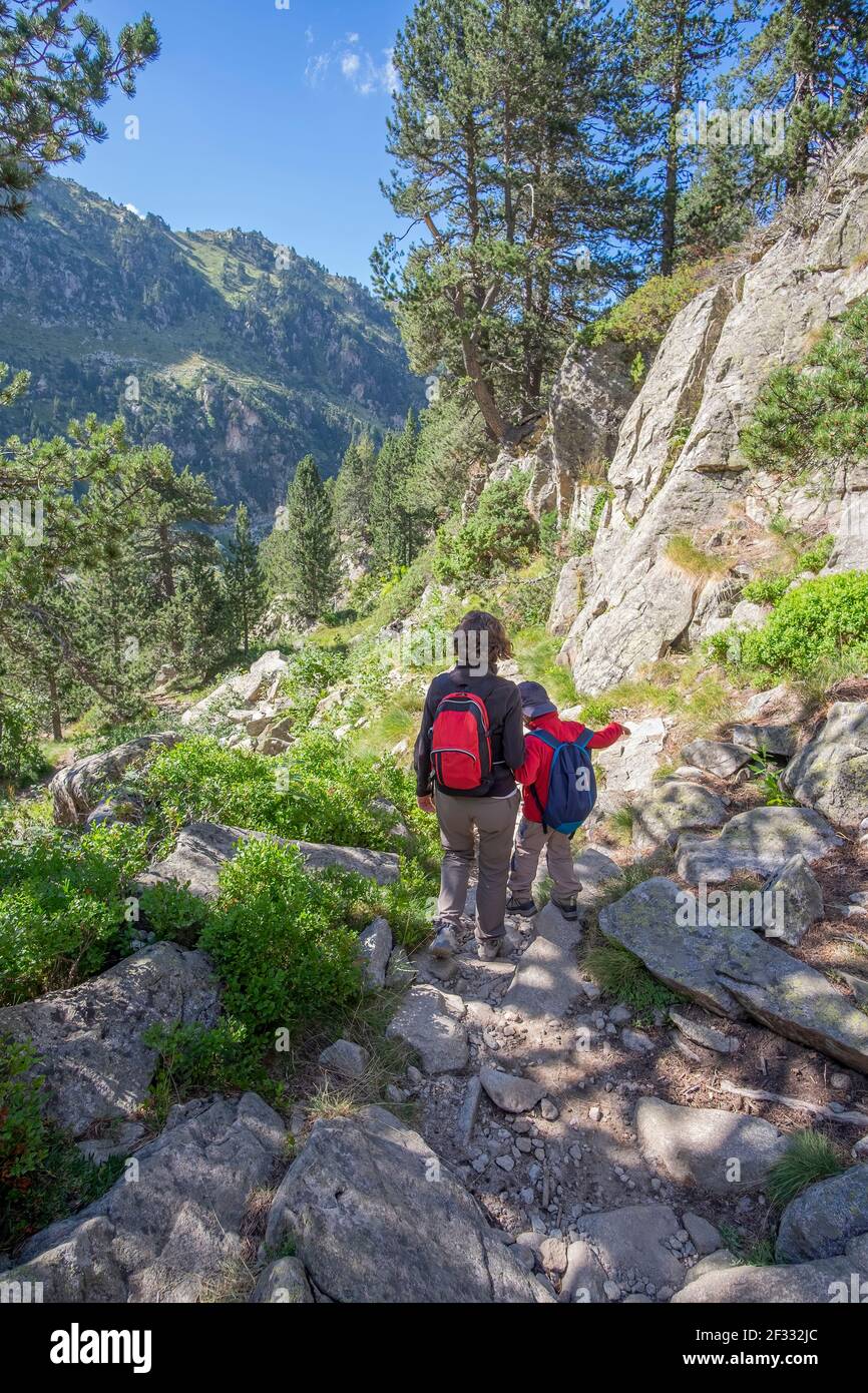 mother and son walk down a mountain trail hand in hand with backpacks and mountain clothing, vertical Stock Photo