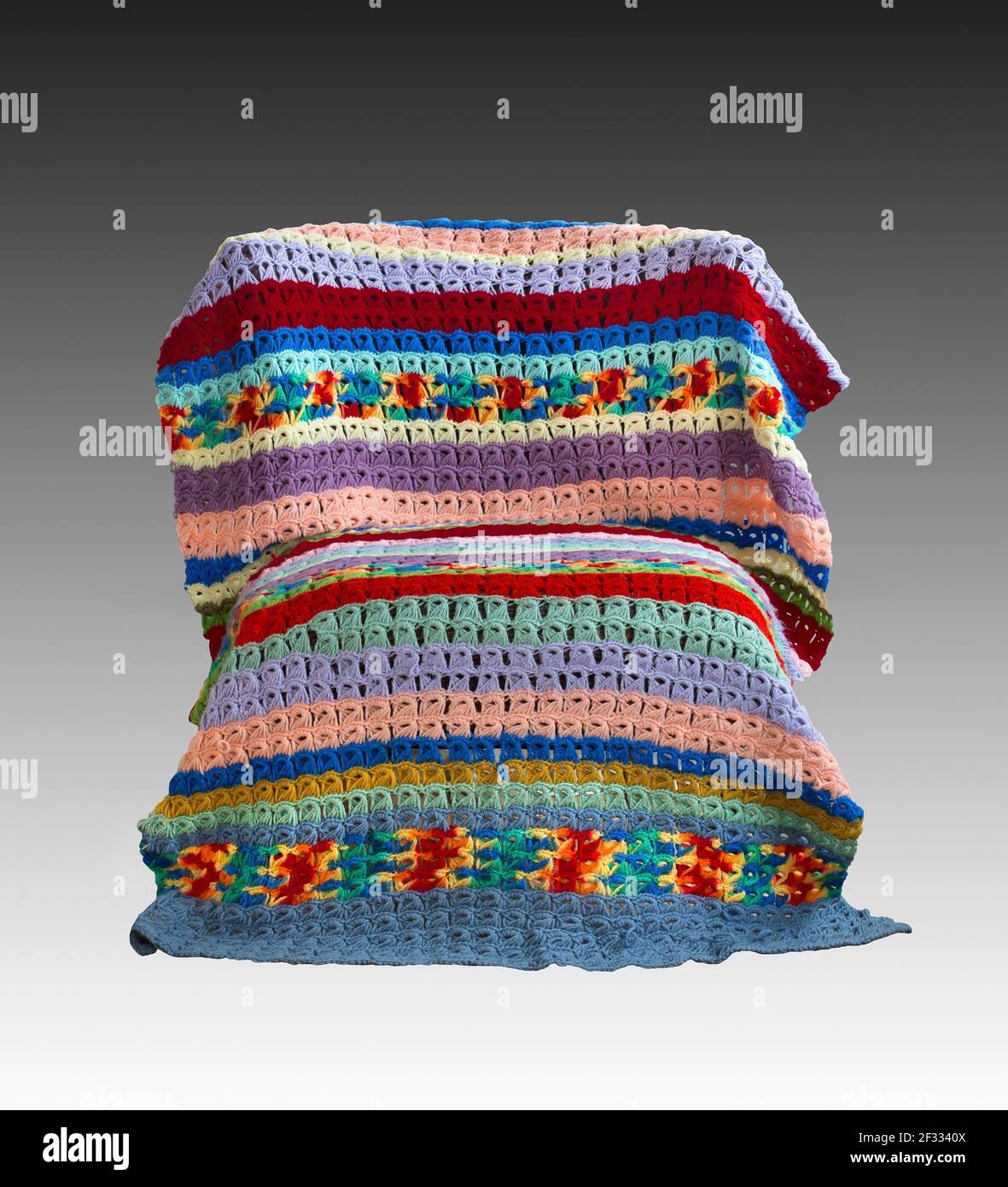 A vintage colorful broomstick stitch lace crochet blanket draped over a chair created by American textile artist Margaret Braaten (1914-2004). Stock Photo