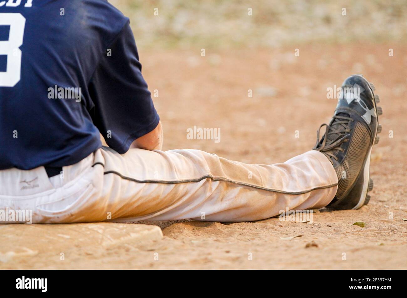 A dirty baseball runner sits on the base after being tagged out on a play. Stock Photo