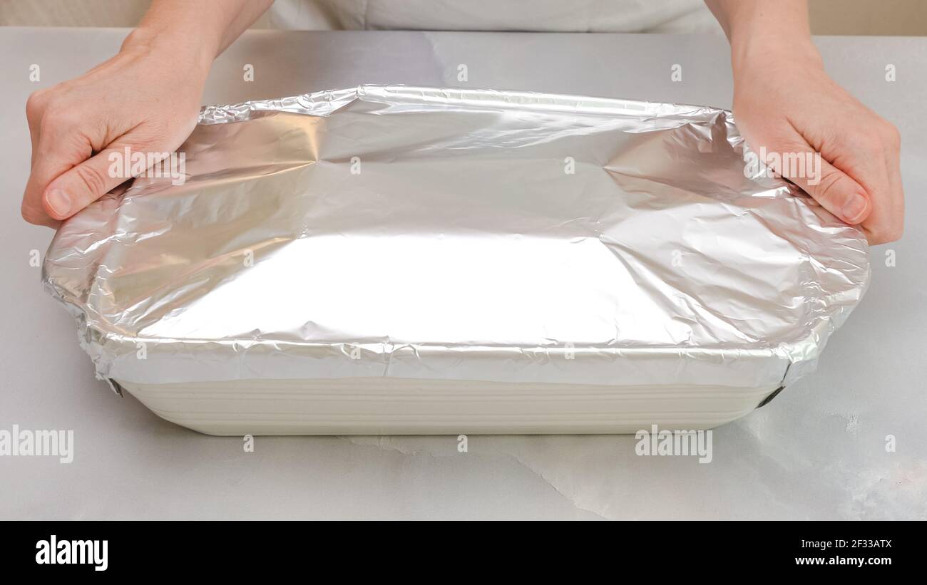 Baking dish covered with aluminum foil. Woman hands, front view, marble