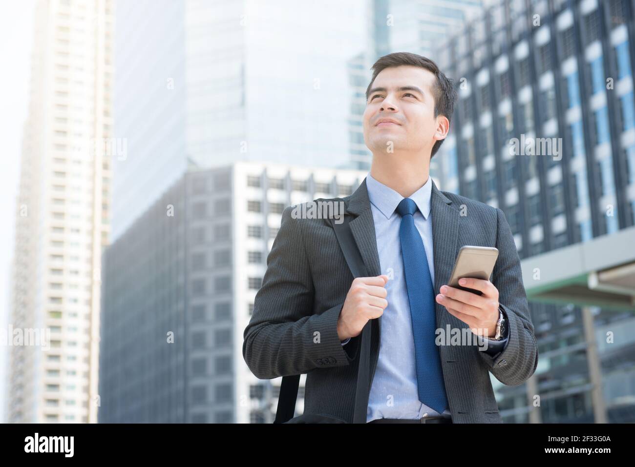 Young businessman using mobile phone while carrying bag in the city - business travel and roaming concepts Stock Photo