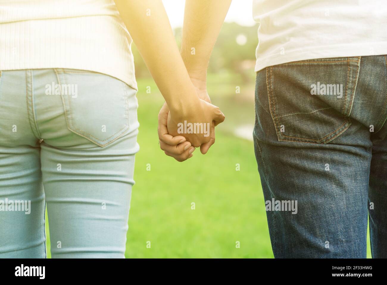 Back view of young casual couple holding hands while walking in the park - dating, love and romance concepts Stock Photo