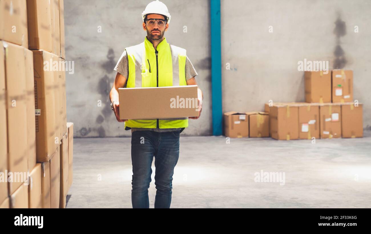 Warehouse worker carrying cardboard box in the warehouse . Packaging delivery and supply chain management concept . Stock Photo
