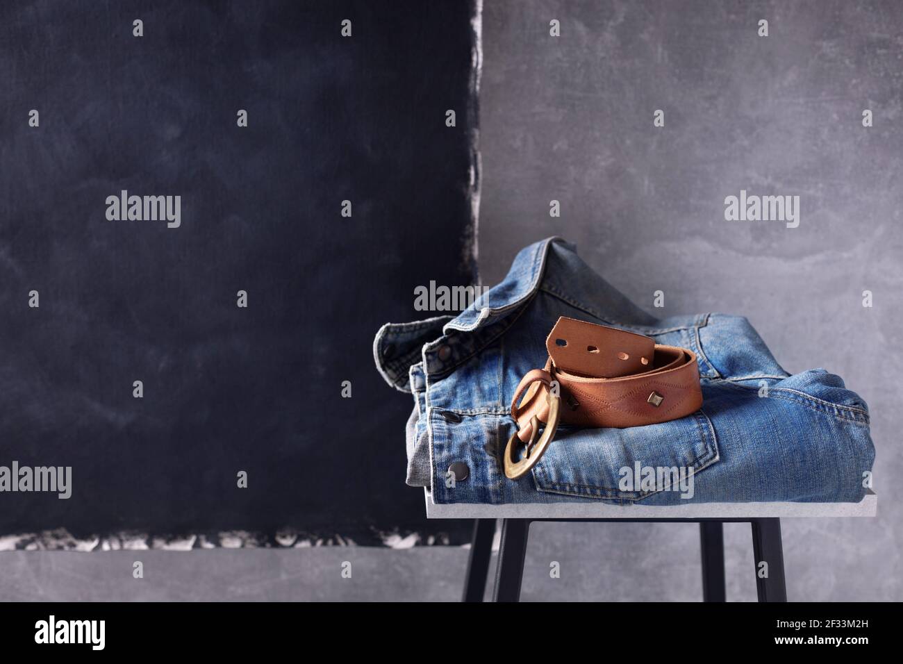 Denim jeans jacket suit and belt at shelf near grey wall background texture. Stack of classic jeans fashion at table Stock Photo