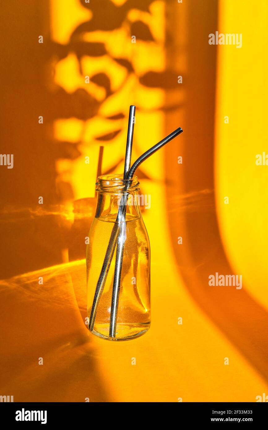 Reusable Metal Straws in glass bottle with water on yellow background