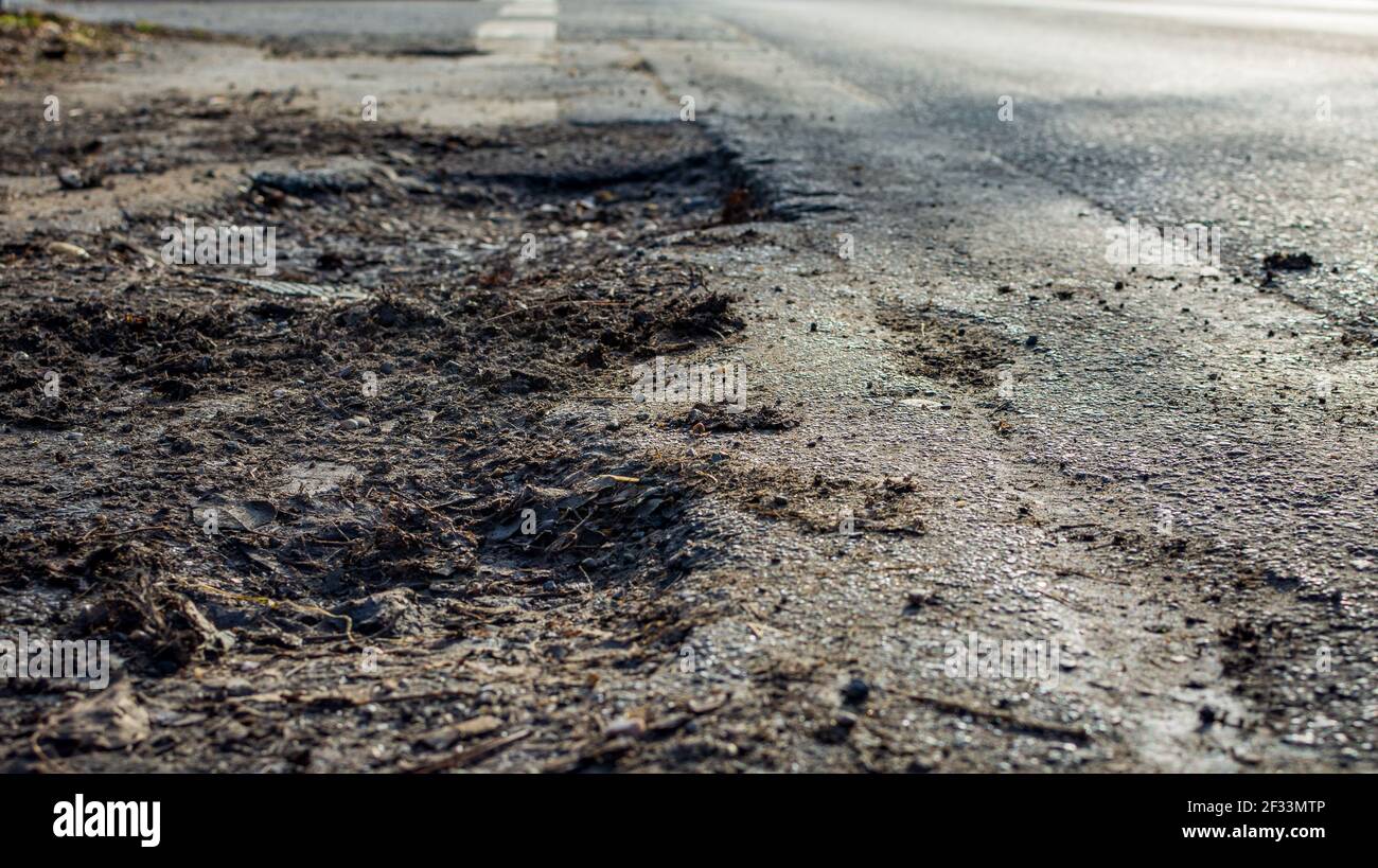 old street with holes. Landscape road with potholes in sunny winter weather. The concept of the absence of timely repair of the street. Damaged infras Stock Photo