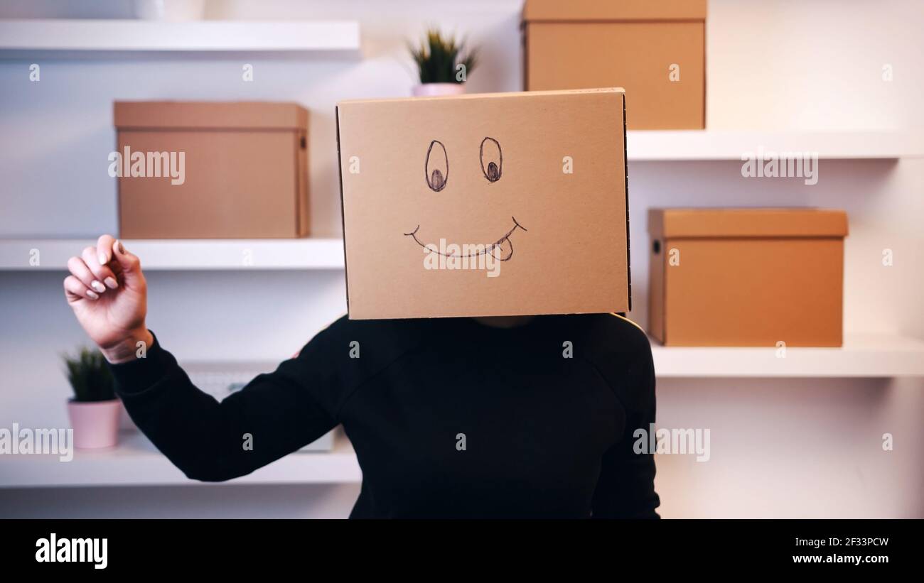 Young happy woman with a cardboard box over head with drawn emoji dancing in the new apartment. High quality photo Stock Photo