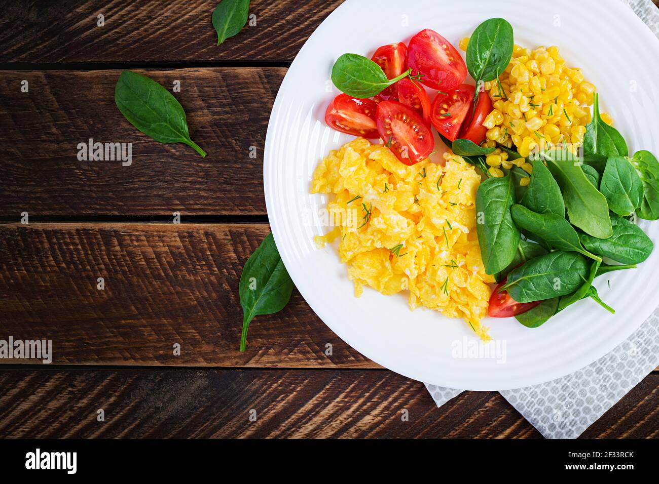 Breakfast. Scrambled eggs with cherry tomatoes, spinach  and corn. Top view, flat lay, above Stock Photo