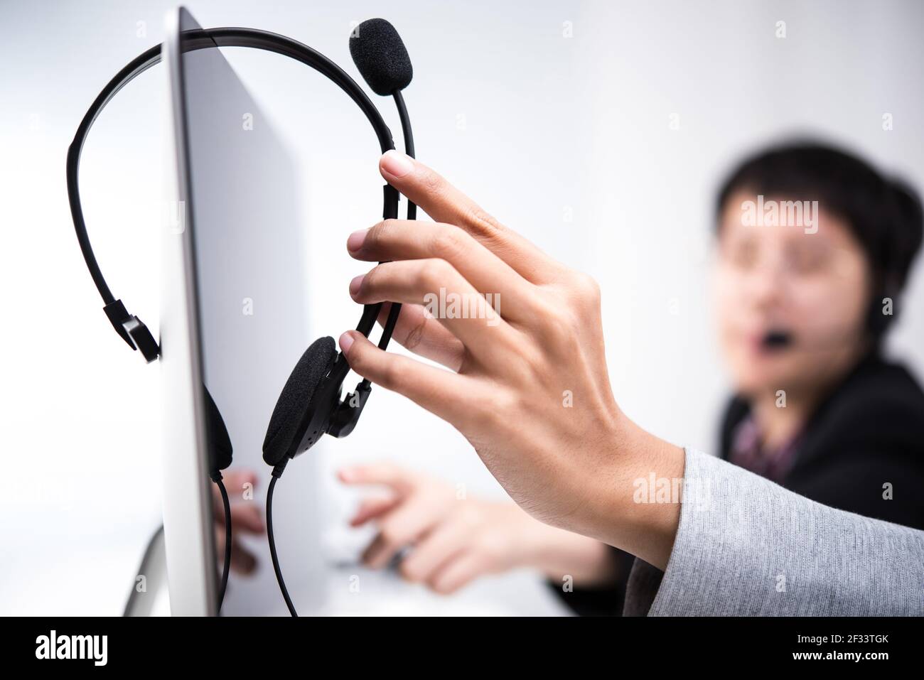 Hand picking up headphone that hanging on computer screen Stock Photo