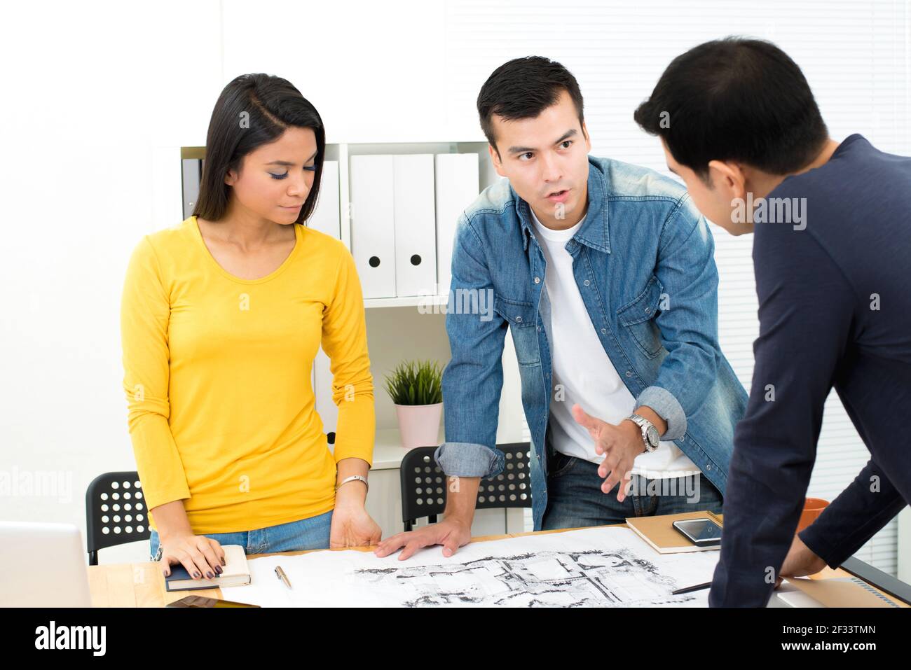 Casual business people (architects or landscape designers) discussing blueprint in the office Stock Photo