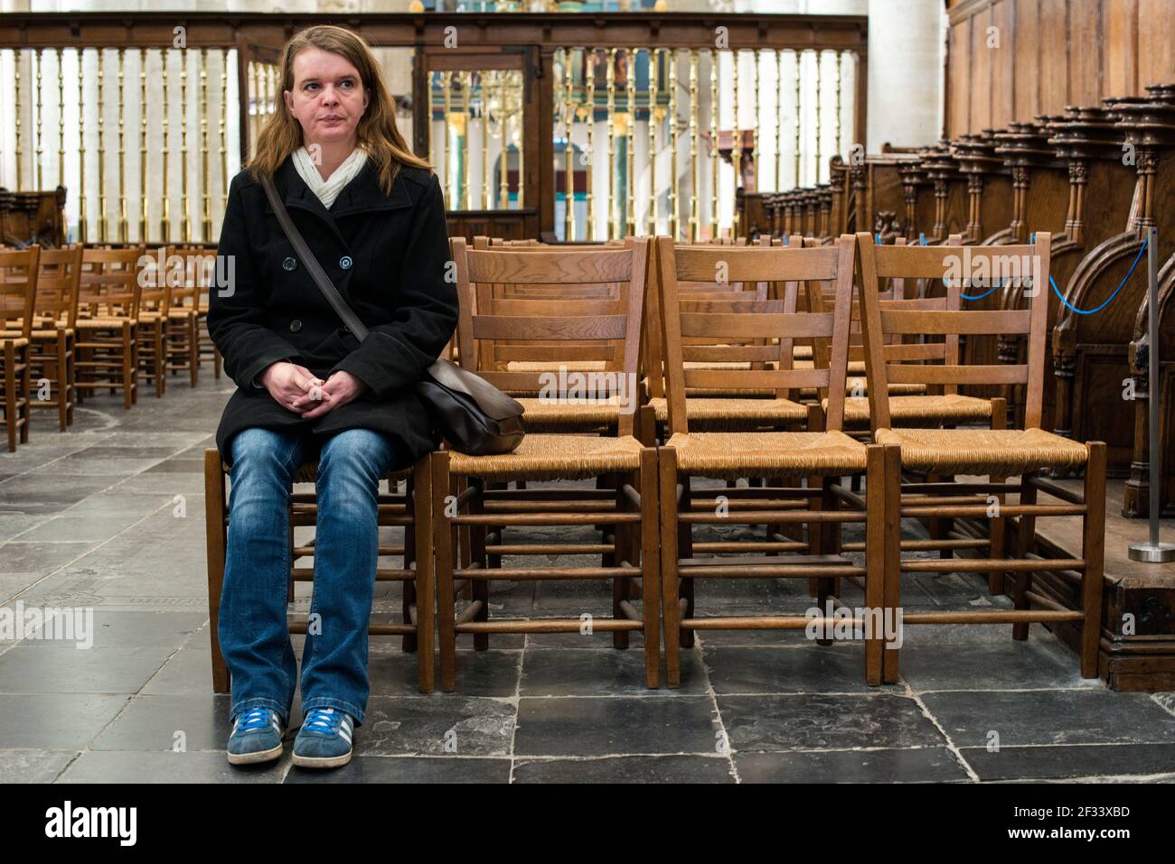Breda, Netherlands. Mid adult caucasian woman contemplating and praying inside a mediaval protestant church. Stock Photo
