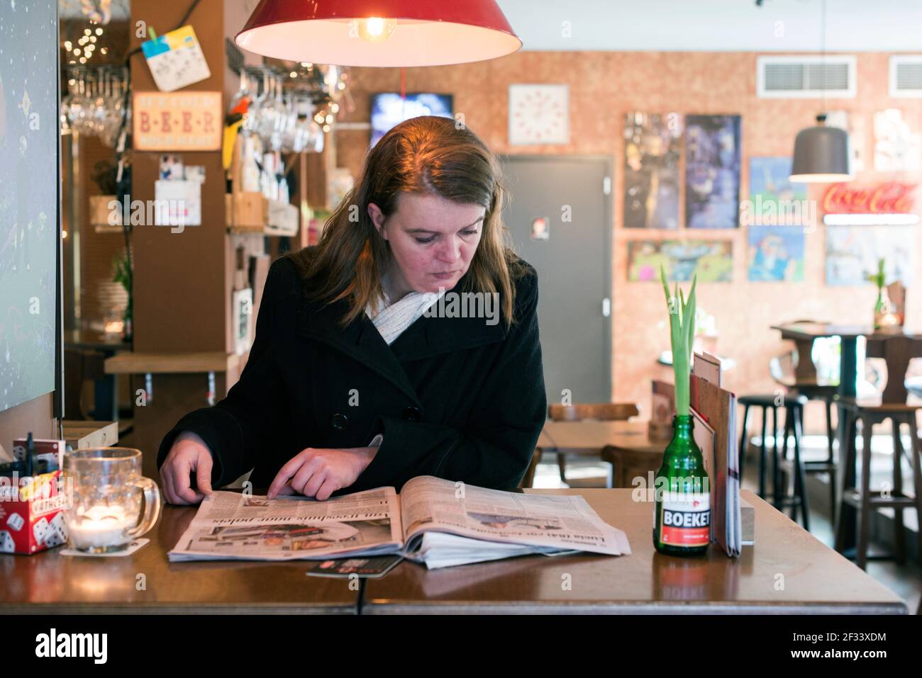 Breda, Netherlands. Mid adutl caucasian woman reading a newspaper while visiting a bar. Stock Photo